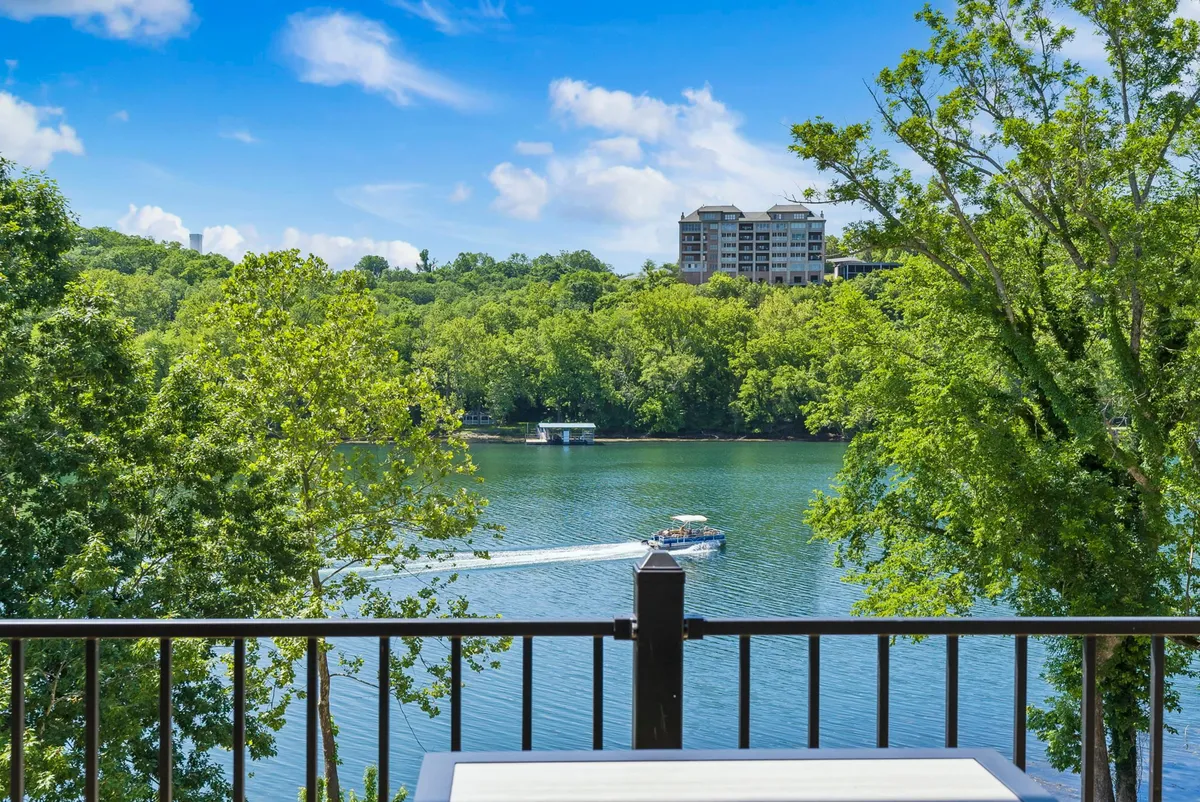 This image features a vibrant view of Lake Taneycomo, with lush greenery bordering calm water. Boating activity and people picnicking can be seen along the lakeshore, immersing the viewer in the tranquil and refreshing lakeside environment.