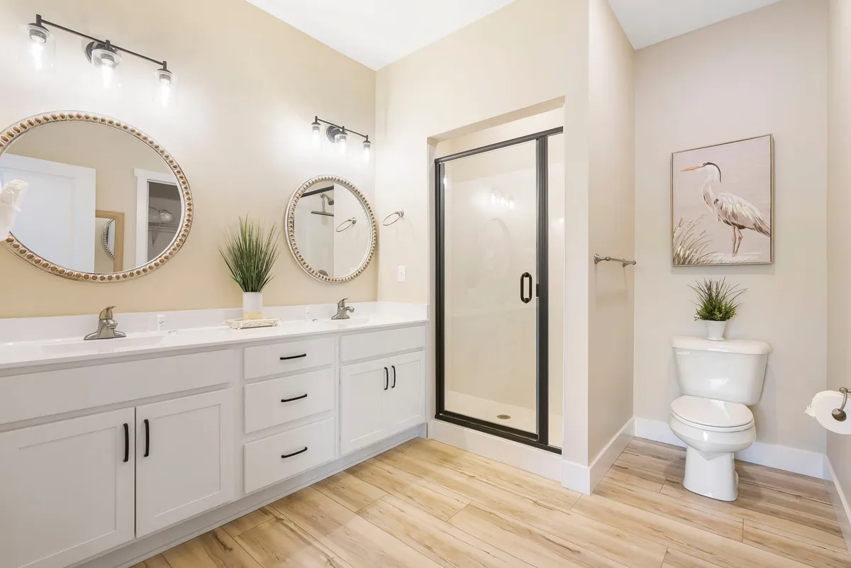 A modern, tranquil bathroom showcasing double sinks, framed mirrors, a walk-in shower, and decorative touches. The space exudes a sense of luxury and relaxation, hinting at spa-like amenities and an elegant self-care environment.