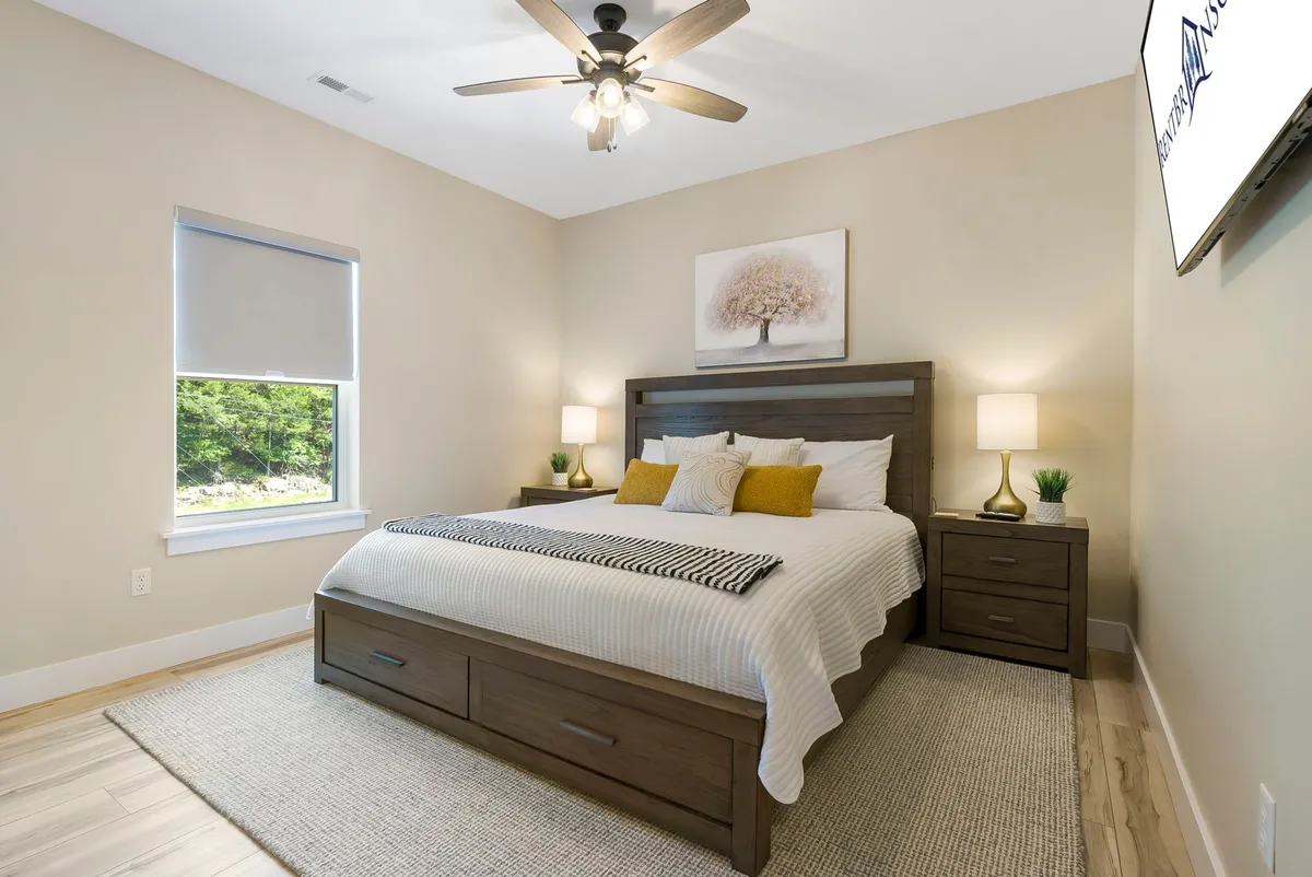 A bright, airy bedroom with a king-sized bed, decorative pillows, dual nightstands with lamps, and a window letting in morning sunlight. The space feels inviting and restful, ideal for unwinding after a day by the lake or with friends and family.