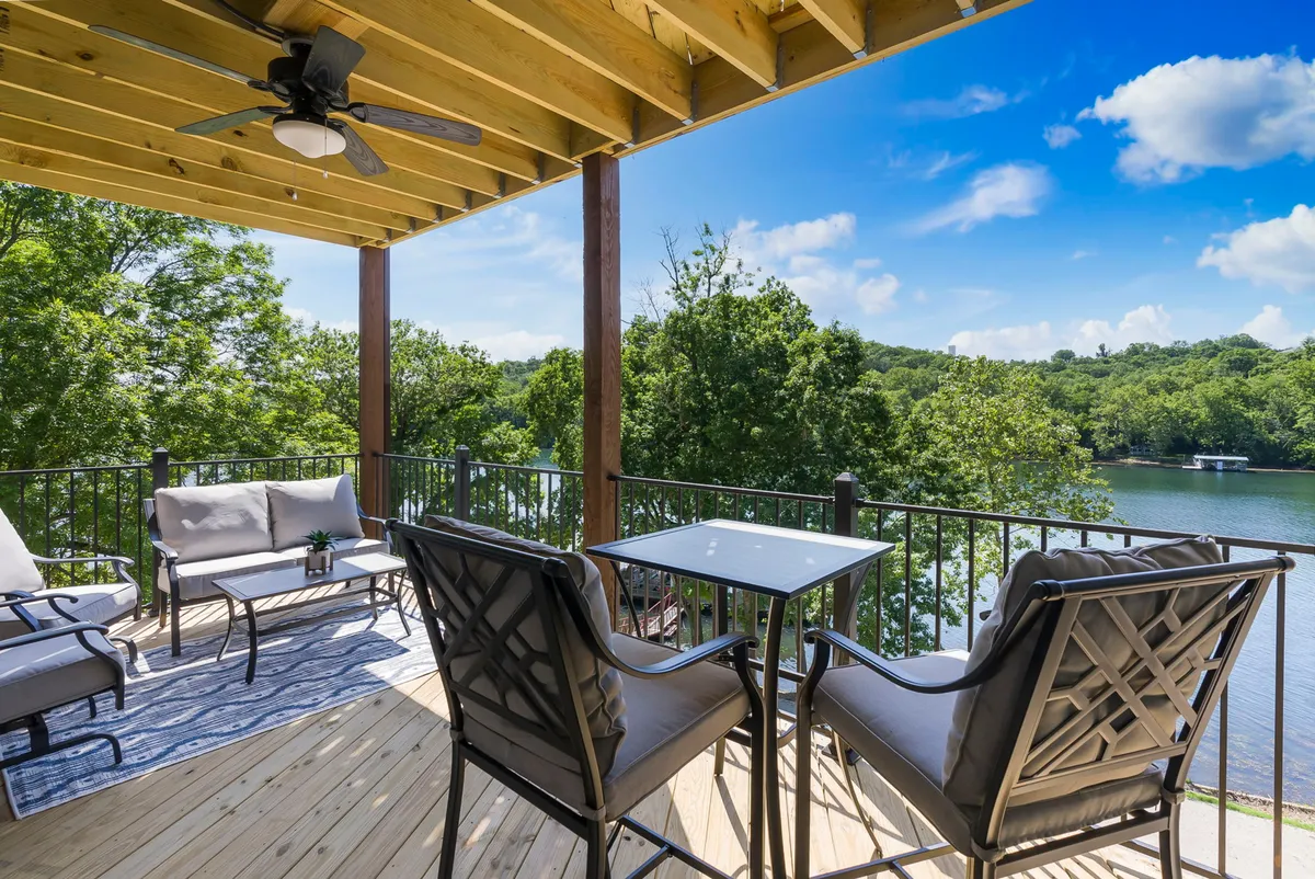 A beautifully arranged outdoor seating area is set on a deck with a stunning view of the water and lush greenery. The scene conveys a sense of relaxation and connection with nature, ideal for both group gatherings and quiet moments. The deck looks spacious and inviting, with comfortable furnishings and room for alfresco dining or lounging.