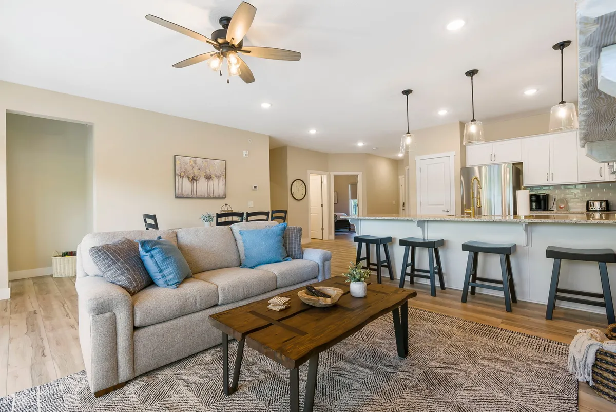 A spacious, open-plan living area featuring a comfortable sofa, a well-appointed coffee table, and a kitchen island illuminated by elegant pendant lights. The scene showcases a welcoming space ideal for relaxing, entertaining, or spending quality time with family.
