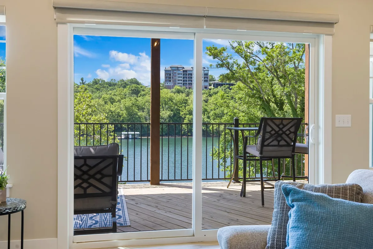 This image captures a large sliding glass door leading out to an outdoor seating area, with a tranquil lake view beyond. The scene shows a peaceful transition from the interior living space to the private deck, featuring inviting chairs perfect for sipping coffee or relaxing while soaking in the scenery.