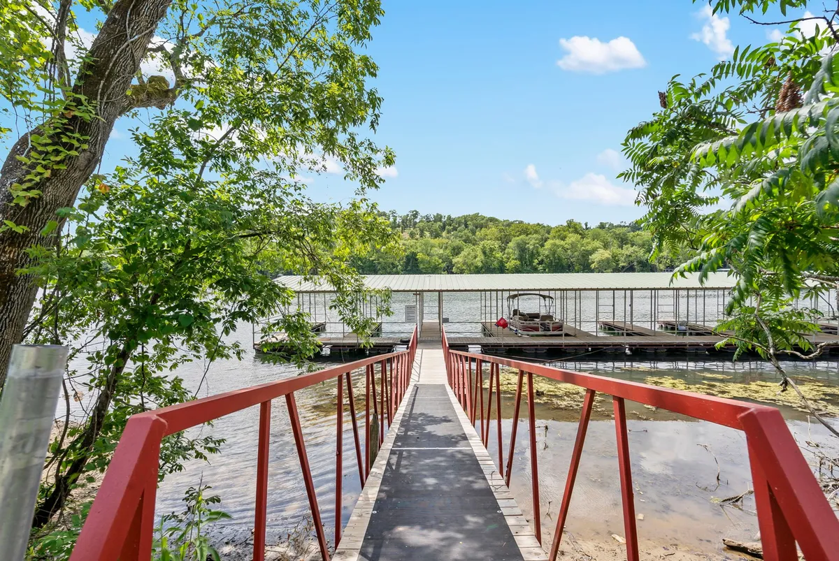 An exterior view showcases a red walkway leading to a dock on the lake, surrounded by greenery. The perspective draws attention to the proximity and accessibility of the water, with the deck area subtly visible, hinting at the seamless connection between the deck and the lakeside environment.
