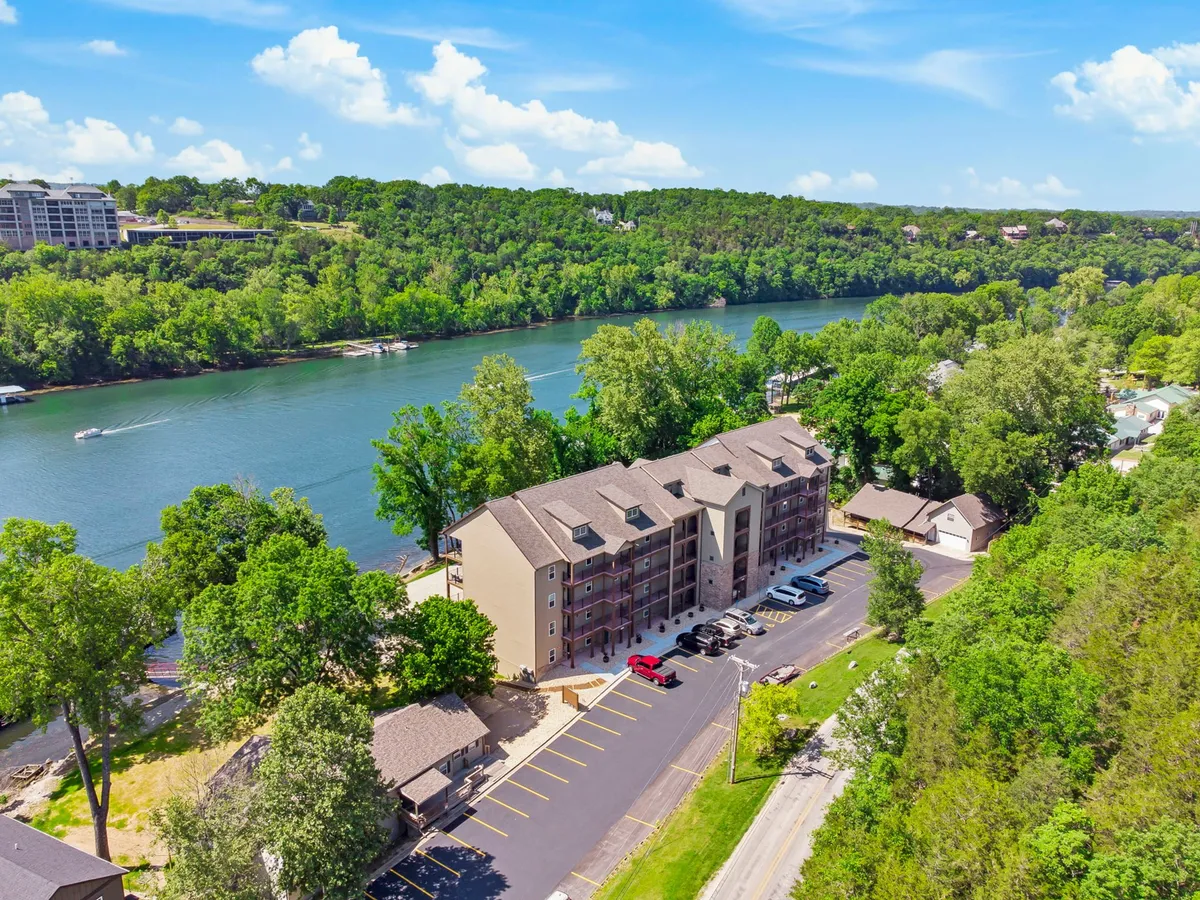 This image offers a wider view of the multi-story condo building nestled alongside the river, framed by lush greenery. The tranquil water and natural surroundings suggest opportunities for boating, fishing, and relaxing after a day in the city, connecting the property directly to outdoor recreational options.