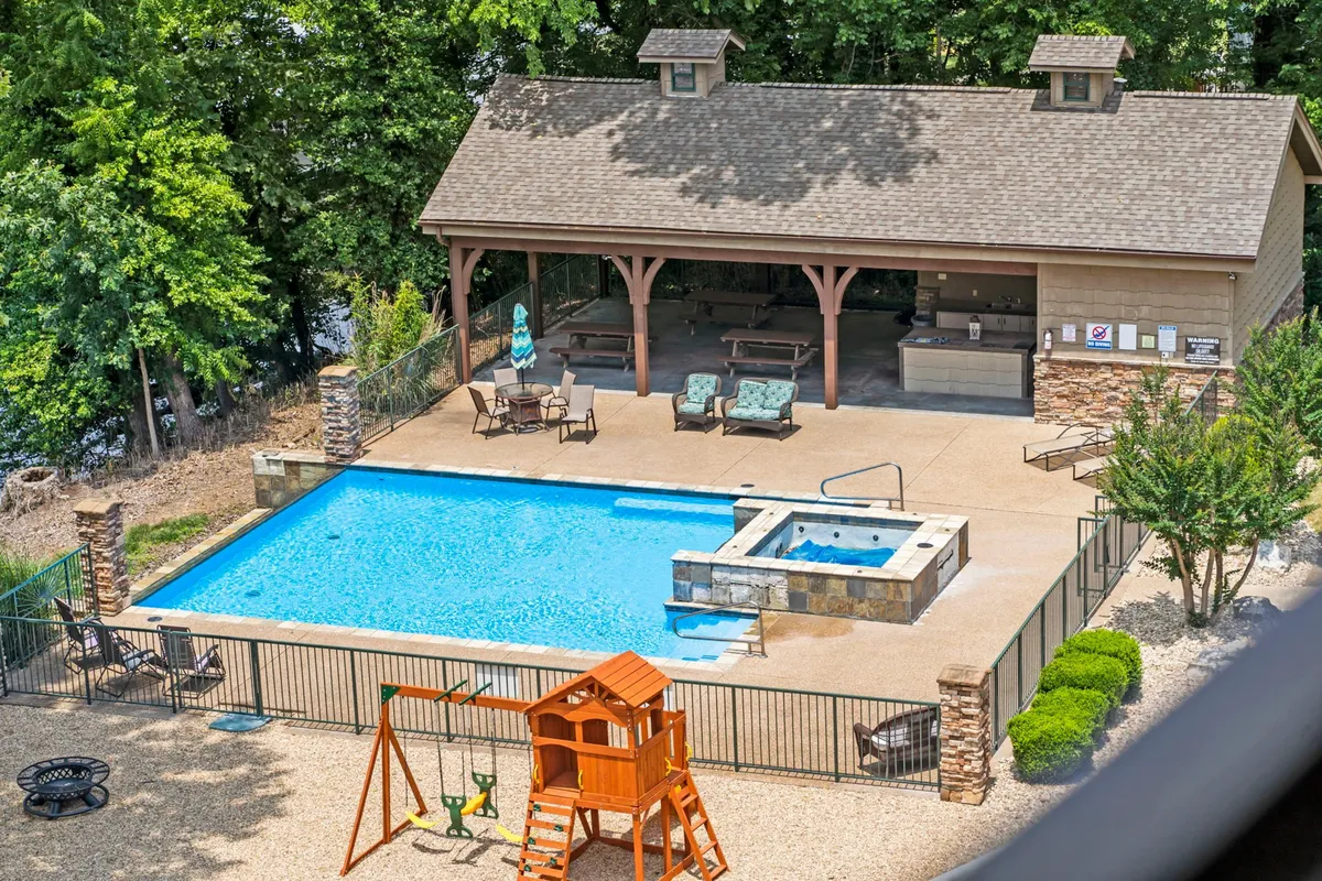 A lively exterior photo of the community’s outdoor pool area, featuring a swimming pool, hot tub, playground, and a covered gazebo. Children play near the playground while friends relax by the pool, all set against a backdrop of sunset lighting.