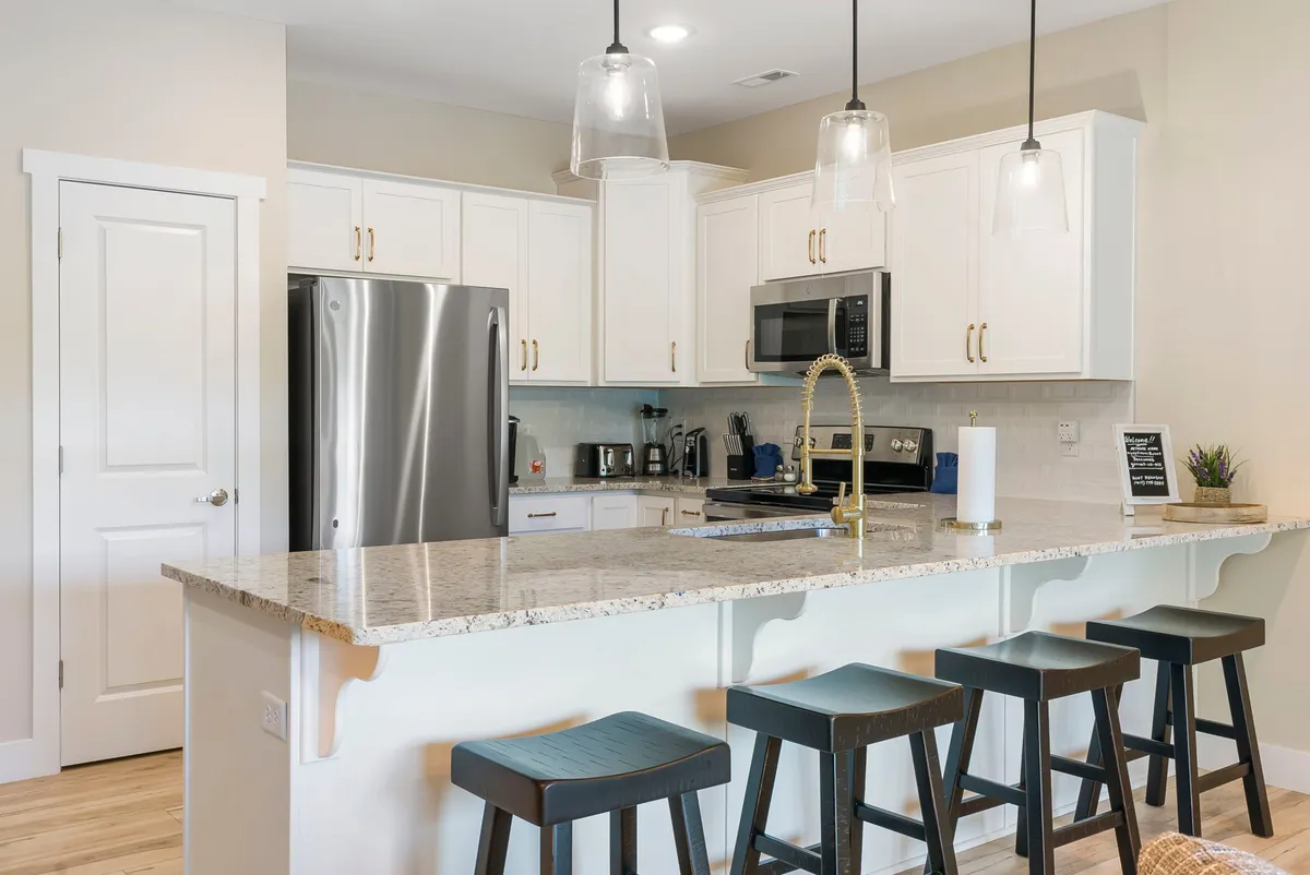 A modern kitchen with a prominent granite countertop, stainless steel appliances, bar stools, and stylish pendant lighting. The space feels functional yet welcoming, ideal for cooking, entertaining, and casual dining.