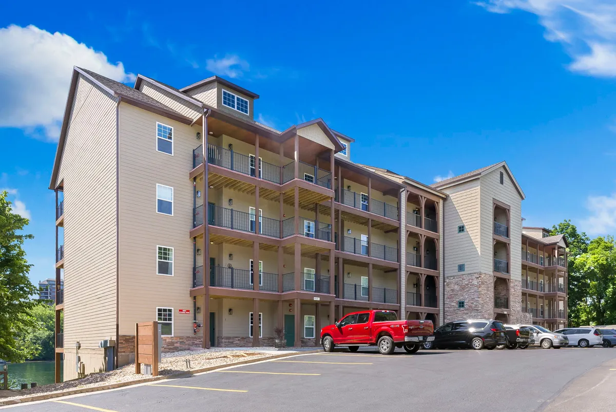 A welcoming exterior view of the building, featuring modern architecture, balconies overlooking lush greenery, and the parking area. The scene suggests a peaceful atmosphere perfect for returning after cultural excursions or outdoor adventures.